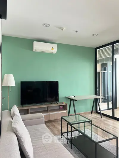 Modern living room with sleek furniture and green accent wall, featuring a TV and air conditioning.