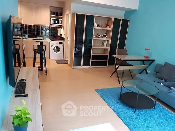 Modern living room with open kitchen and washing machine, featuring stylish furniture and vibrant decor.