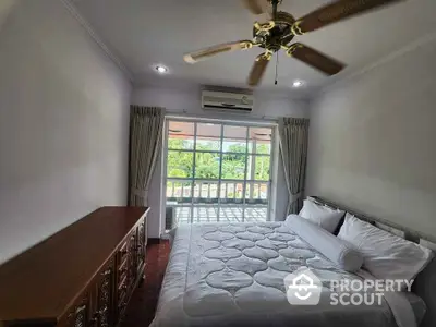 Cozy bedroom with large window and ceiling fan, offering a serene view and ample natural light.