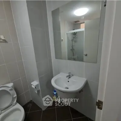 Modern bathroom with sleek fixtures and neutral tiles, featuring a shower and compact sink area.