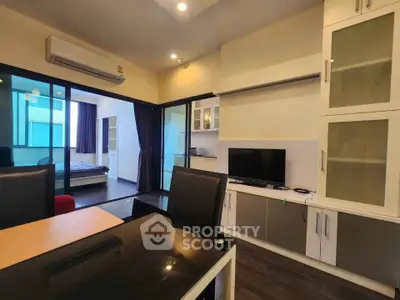 Modern apartment interior with open living room and bedroom view, featuring sleek furniture and glass cabinets.