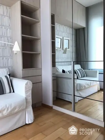 Elegant bedroom with mirrored wardrobe reflecting a plush bed, crisp white decor, and built-in shelving, creating a serene and spacious atmosphere.