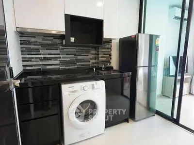 Modern kitchen with sleek black cabinets and appliances, featuring a washing machine and fridge.