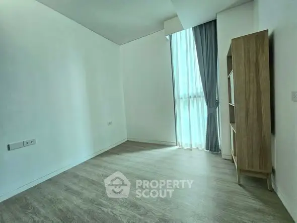 Spacious empty room with wooden flooring and natural light from large window.