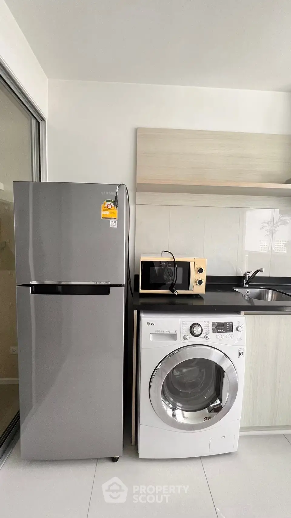 Modern kitchen with sleek appliances including fridge, washing machine, and microwave in a compact layout.