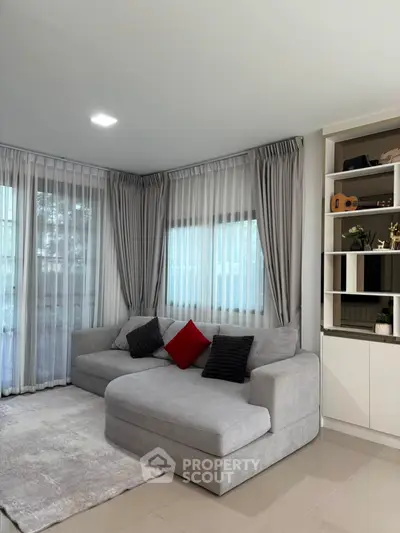 Modern living room with stylish gray sofa, elegant curtains, and built-in shelving for a cozy ambiance.