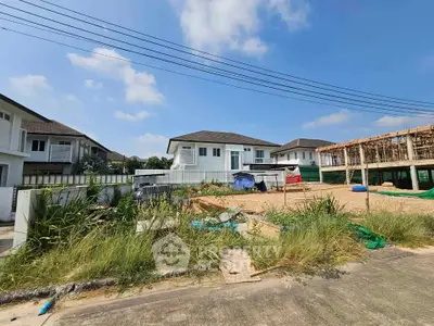 Spacious residential plot with modern houses and clear blue sky, ideal for new home construction.