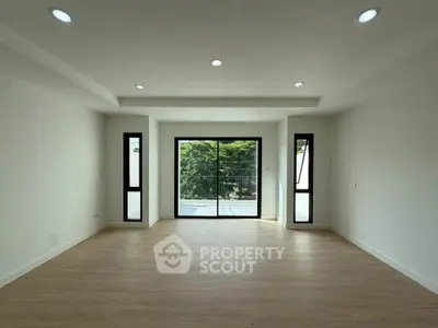 Spacious empty living room with large windows and wooden flooring, perfect for customization.