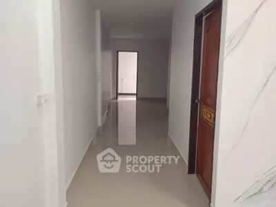 Spacious hallway with glossy tiled floors and elegant wooden door, leading to a bright open area.
