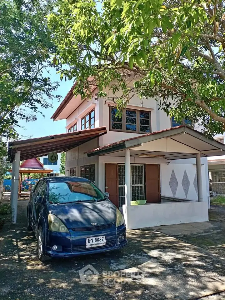 Charming two-story house with carport and lush greenery, perfect for family living.