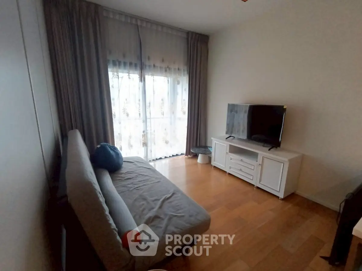 Cozy living room with sofa and TV, featuring large window with curtains.