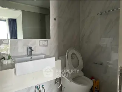 Modern bathroom with sleek fixtures and marble walls, featuring a stylish sink and toilet.