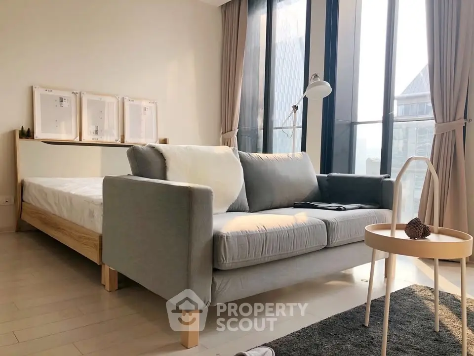 Modern bedroom with stylish sofa and large windows offering natural light and city views.