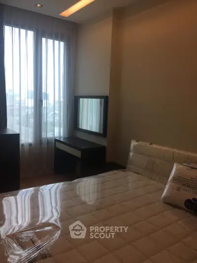 Cozy bedroom with large window and modern furnishings in a high-rise apartment.