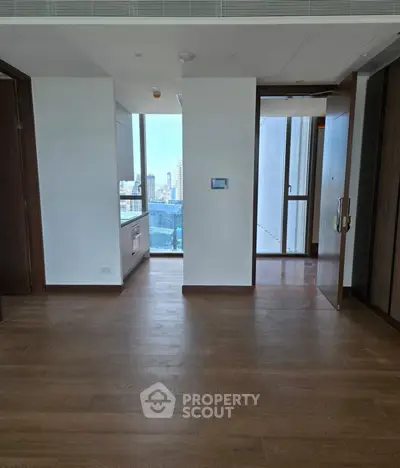 Modern apartment interior with wooden flooring and city view, featuring a compact kitchen area.
