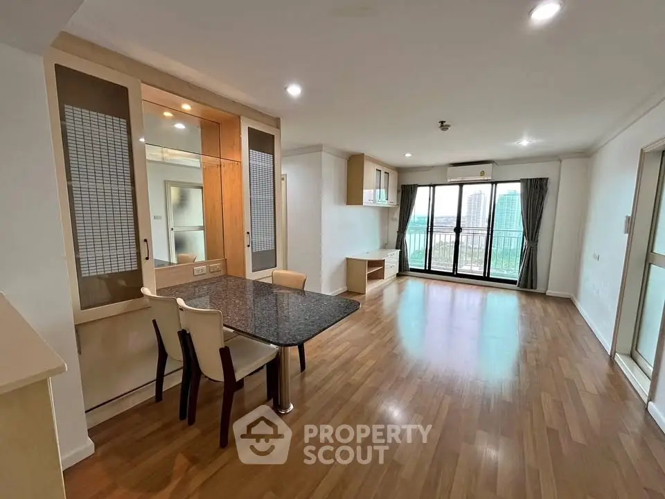 Spacious modern living room with hardwood floors and large windows offering city views.