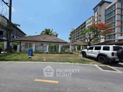 Charming single-story house with tiled roof and lush garden, adjacent to modern high-rise building.