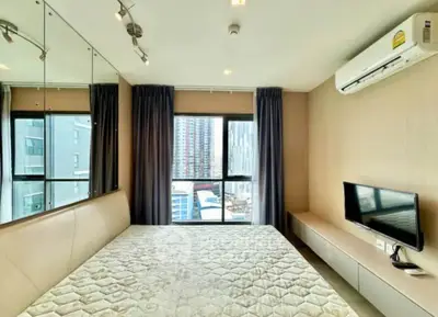 Modern bedroom with large windows and city view, featuring air conditioning and wall-mounted TV.