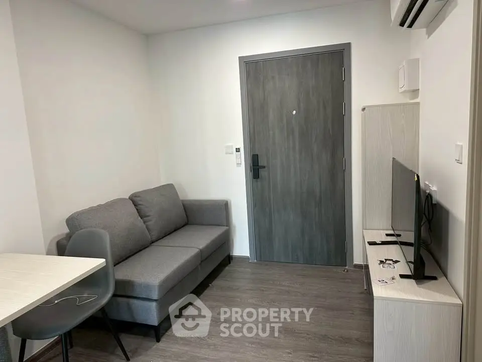 Modern compact living room with gray sofa, TV, and air conditioning in a cozy apartment.