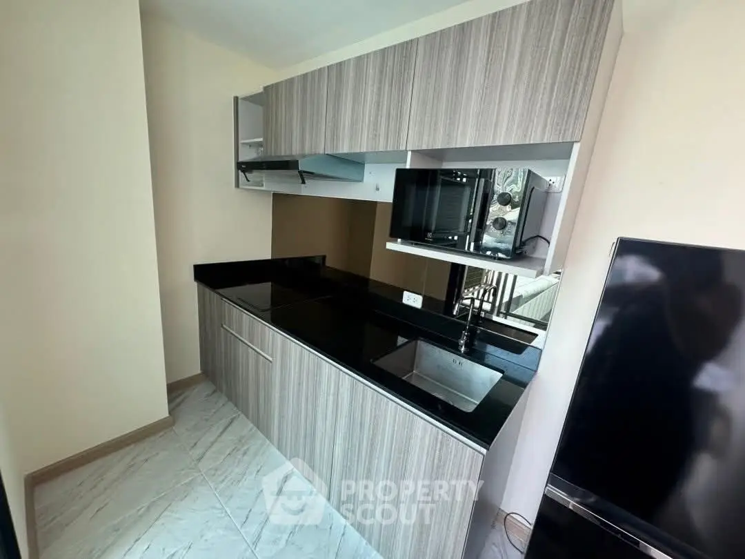 Modern kitchen with sleek cabinetry and black countertops, featuring a built-in microwave and compact design.