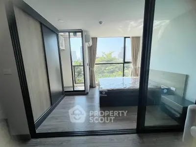 Modern bedroom with large windows and sliding glass doors offering a scenic view, featuring sleek wooden flooring.