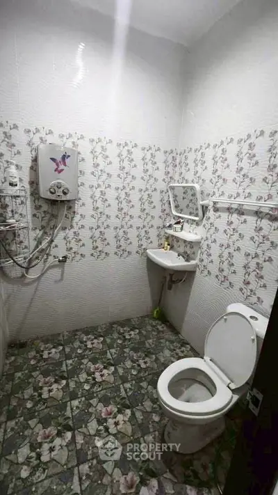 Charming bathroom with floral tiles and compact design, featuring a wall-mounted water heater and essential fixtures.