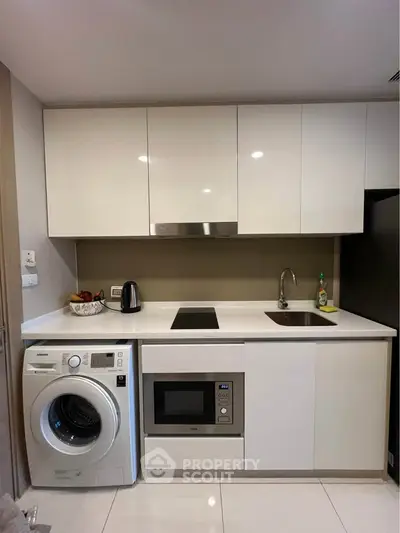 Modern kitchen with sleek appliances and white cabinetry, featuring a washing machine and microwave.