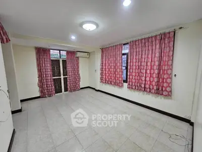 Spacious living room with tiled flooring and large windows, featuring pink curtains and air conditioning.