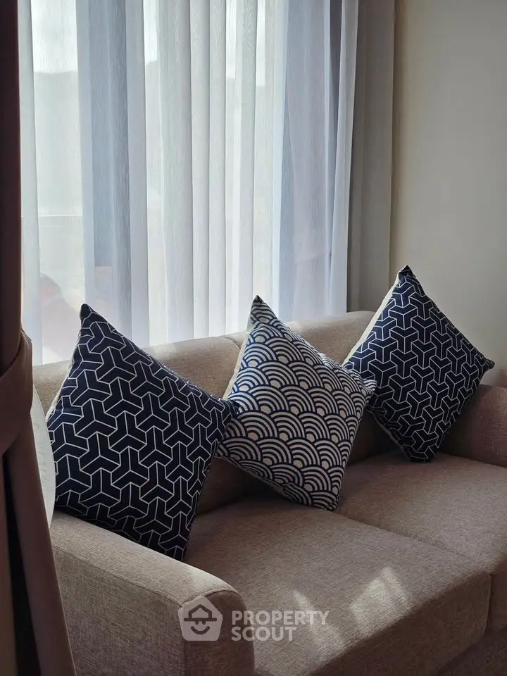 Cozy living room with stylish geometric pillows on a beige sofa by a sunlit window.