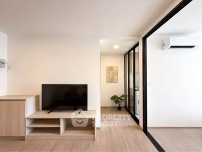 Modern living room with sleek TV stand and glass partition leading to a bright space with air conditioning.