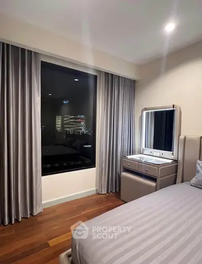 Luxurious bedroom with elegant drapes and city view, featuring modern vanity and cozy ambiance.