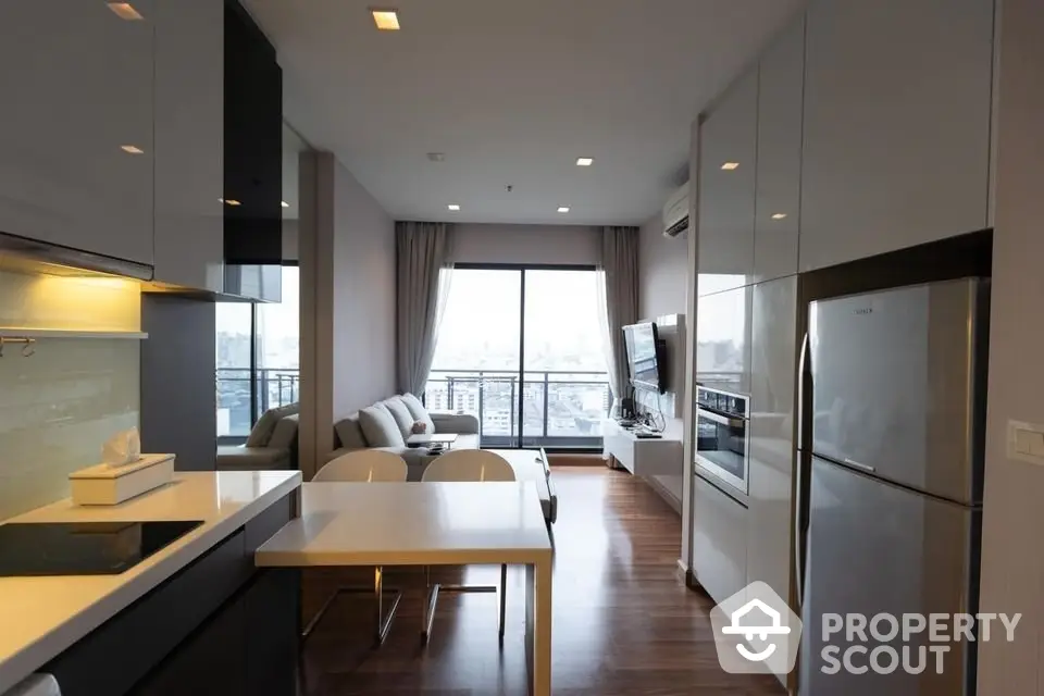 Sleek modern kitchen with stainless steel appliances flows into a cozy living area with abundant natural light and city views, perfect for urban living.