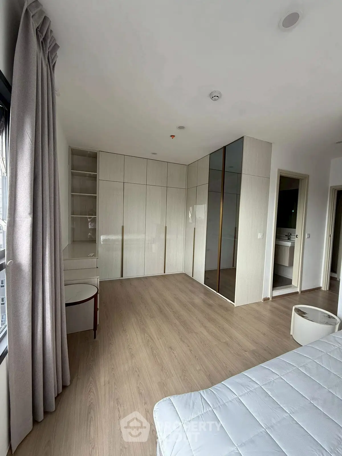 Spacious bedroom with modern built-in wardrobe and large window view.