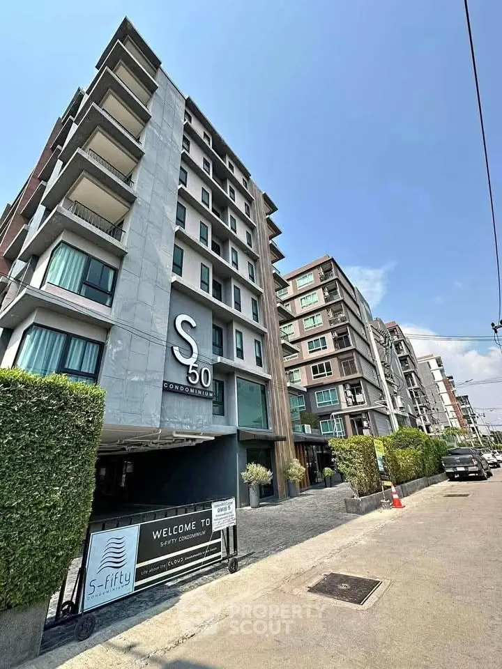 Modern condominium building exterior with lush greenery and clear blue sky.