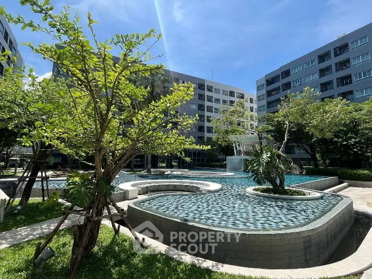 Modern apartment complex with lush garden and stylish pool under clear blue sky.