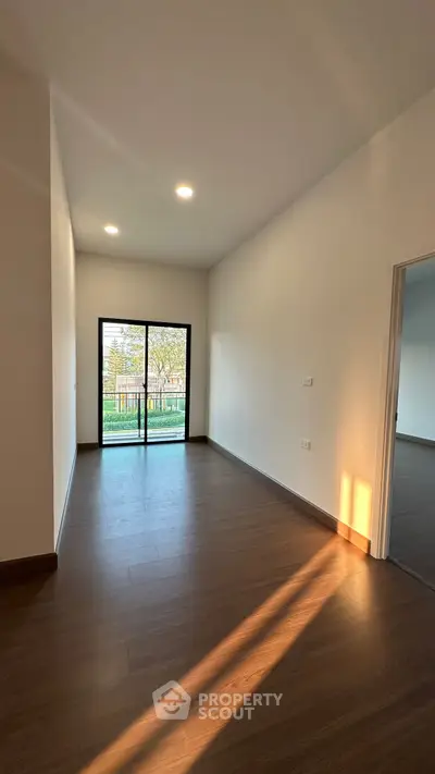 Spacious empty room with wooden flooring and large window overlooking garden.