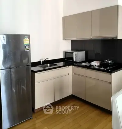 Modern kitchen with sleek cabinets, stainless steel fridge, and wooden flooring in a stylish apartment.