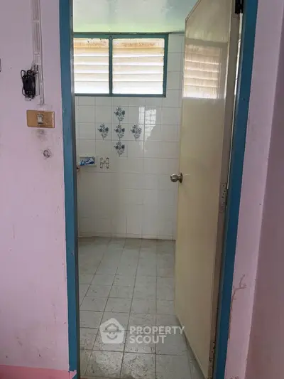 Simple bathroom with tiled walls and floral accents, featuring a partially open door and natural light from windows.