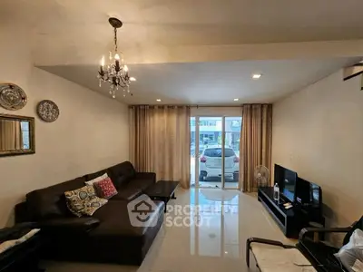 Spacious living room with elegant chandelier and modern furniture, featuring a large window with a view of parked cars.