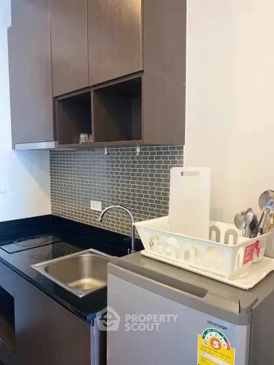 Modern kitchen with sleek cabinets, compact fridge, and stylish backsplash in a cozy apartment.