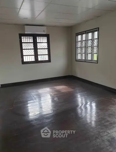 Spacious empty room with dark wooden floors and large windows, perfect for customization.