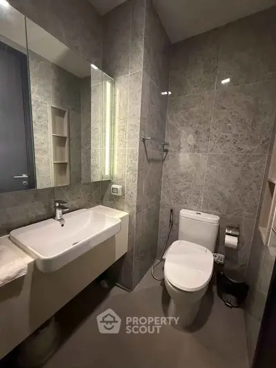 Modern bathroom with sleek fixtures and elegant gray tiles, featuring a spacious sink and contemporary toilet.