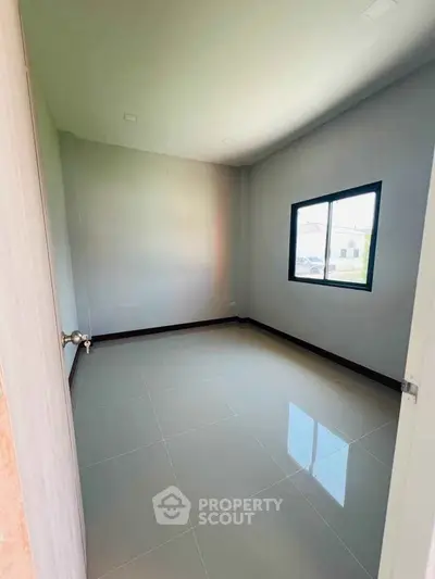 Spacious empty room with glossy tiled floor and large window, perfect for customization.