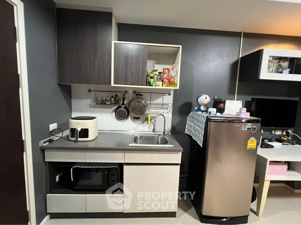 Modern kitchen with sleek cabinets, stainless steel fridge, and compact appliances.
