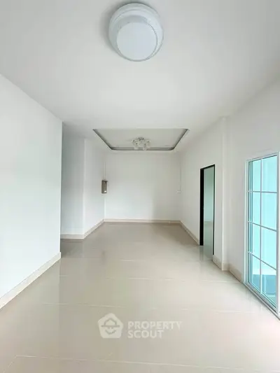 Spacious empty room with modern ceiling light and large window, ideal for customization.