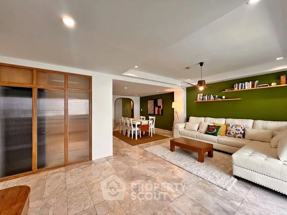 Spacious living room with modern decor and open dining area, featuring elegant lighting and stylish furnishings.
