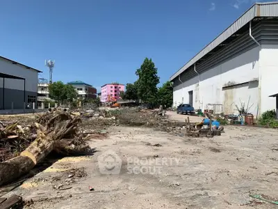 Vacant industrial land with potential for development, featuring clear skies and surrounding buildings.