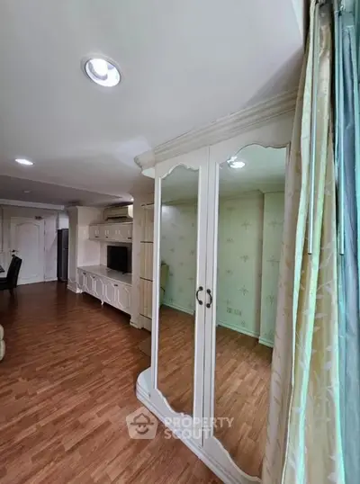 Spacious living room with elegant wooden flooring and mirrored wardrobe, perfect for modern living.