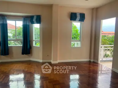 Spacious room with polished wooden floors and large windows opening to a balcony with lush views.