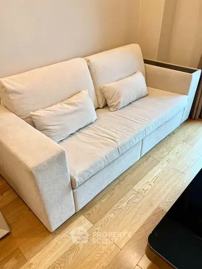 Cozy beige sofa in a modern living room with wooden flooring, perfect for relaxation and comfort.